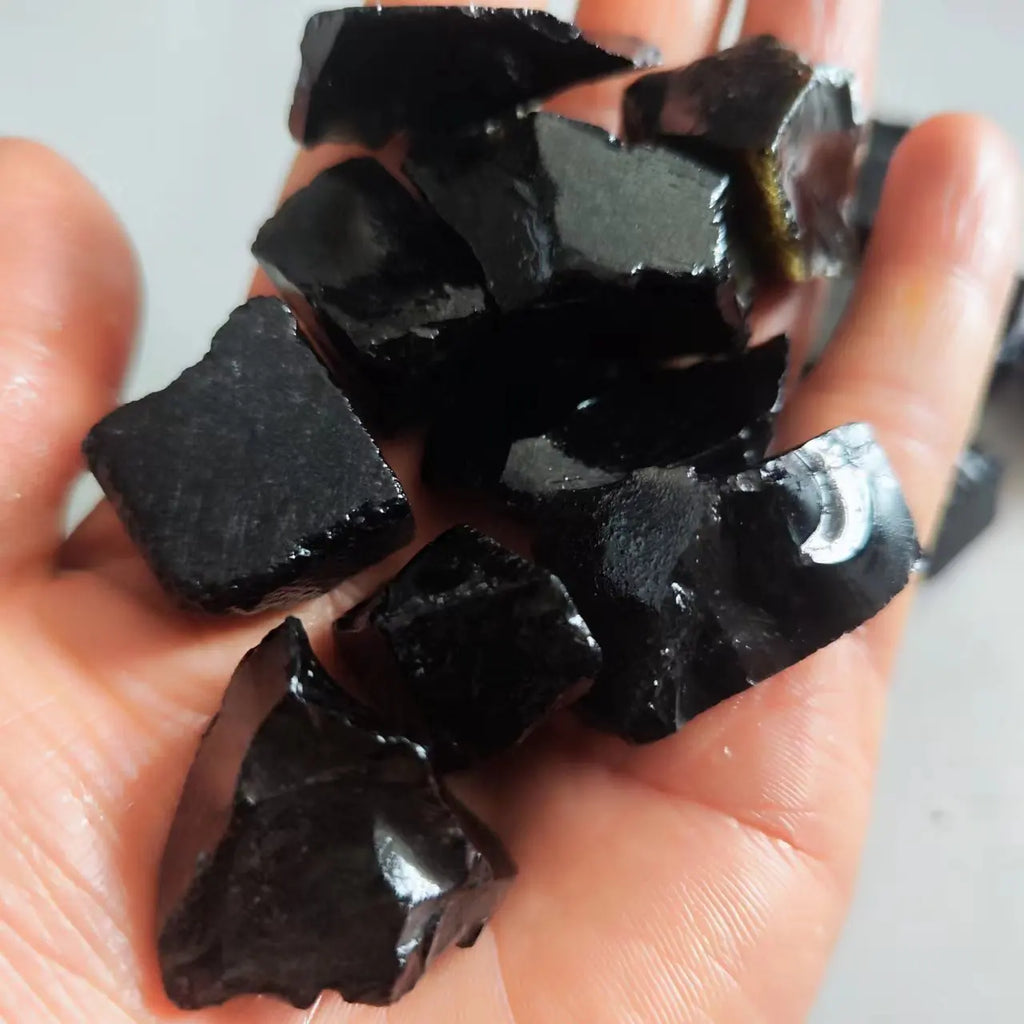 Hand holding a collection of dark, glossy stones against a neutral background
