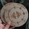 Wooden circular object with engraved designs and butterfly illustrations, held by a hand.