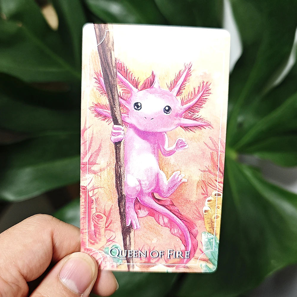 Card featuring a pink axolotl with 'Queen of Fire' text held by a hand against a leafy background