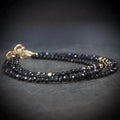 Black beaded necklace with gold clasp on a dark surface