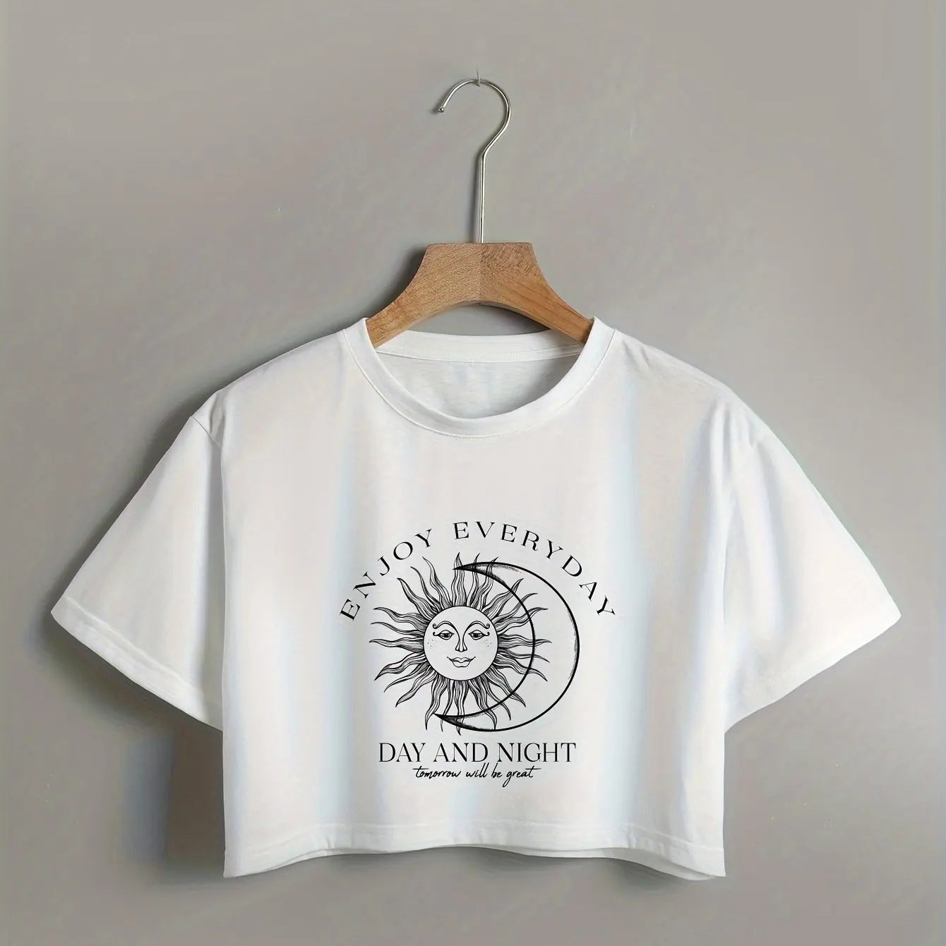 White crop top with sun and moon design and text on a hanger against a gray background