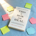 Book titled 'This is How You Heal' by Brianna Wiest on a blue surface with colorful sticky notes.