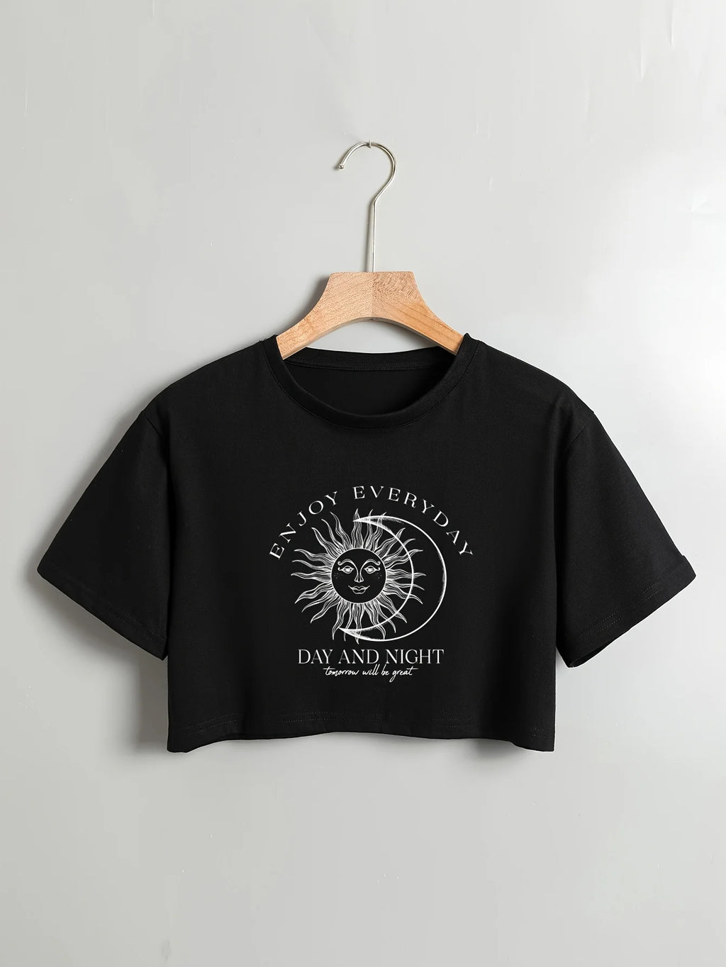 Black crop top with sun and moon design and text on a hanger against a light gray background