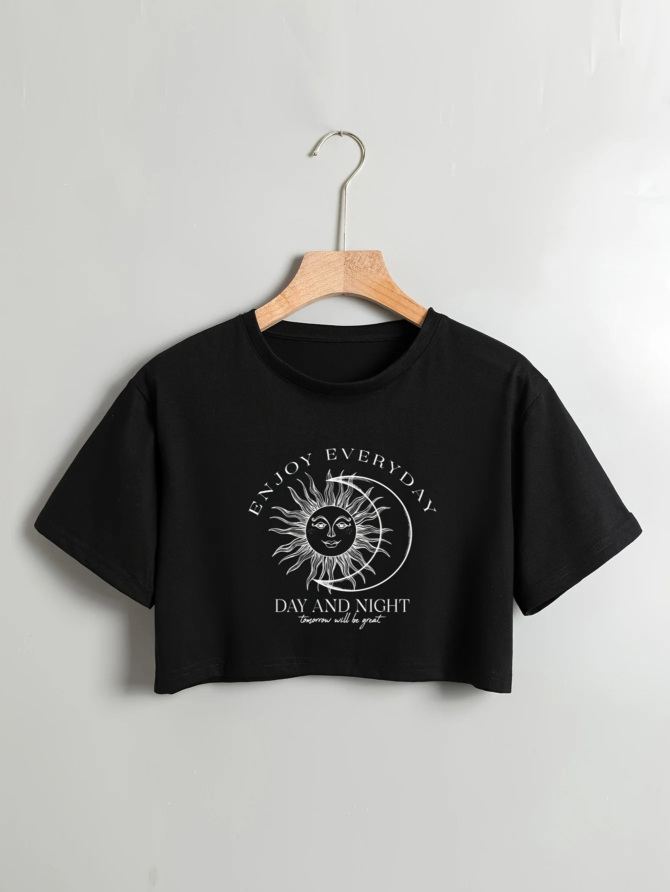 Black crop top with sun and moon design and text on a hanger against a light gray background