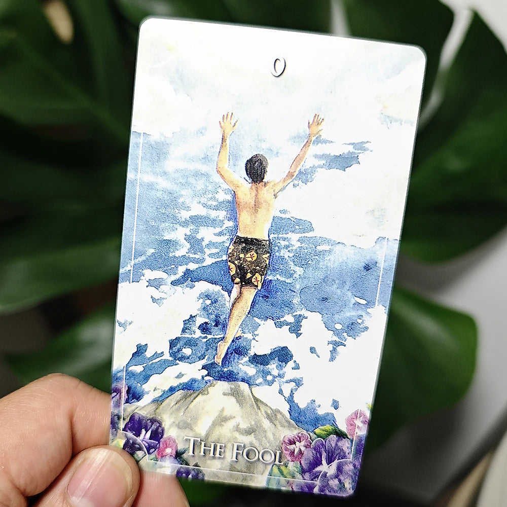 Card featuring a person diving into water with 'The Fool' text, held by a hand against a blurred green leafy background.