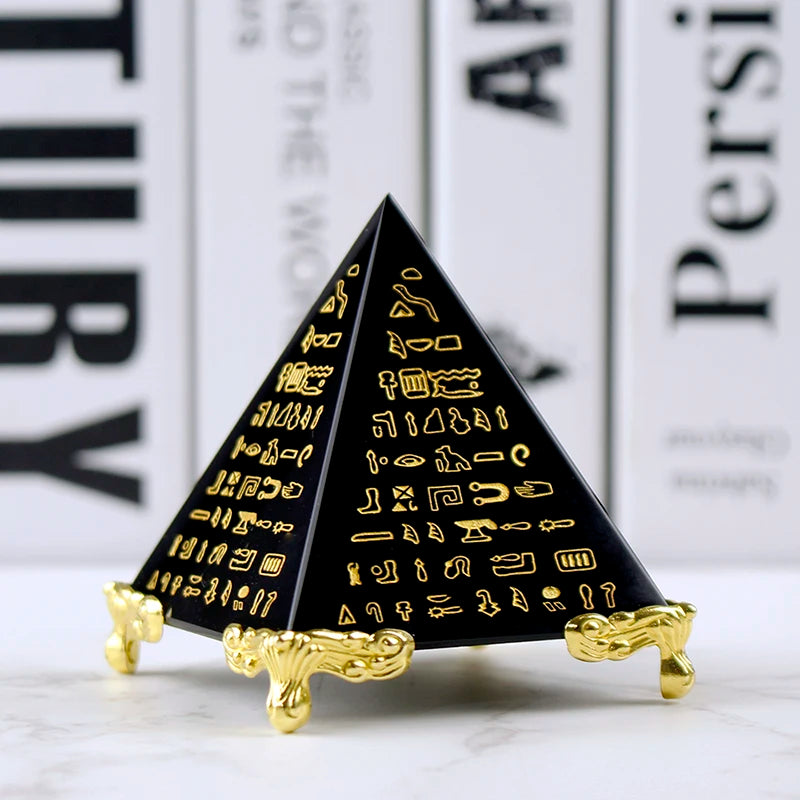 Black pyramid-shaped object with gold hieroglyphics on a white surface