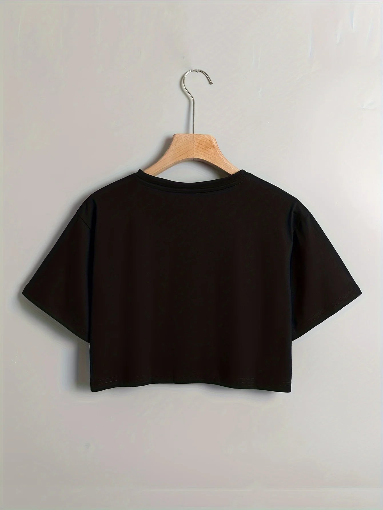 Black crop top on a wooden hanger against a light gray background