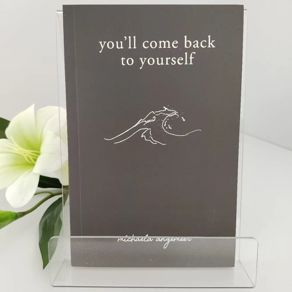 Book titled 'you'll come back to yourself' by Michaela Angerer with a white flower in the background.