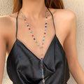 Woman wearing a black strappy top with a colorful beaded necklace against a neutral background
