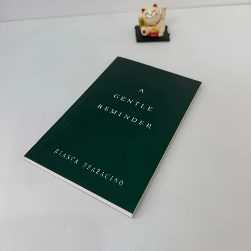 Book titled 'A Gentle Reminder' by Bianca Sparacino on a white surface with a small figurine.
