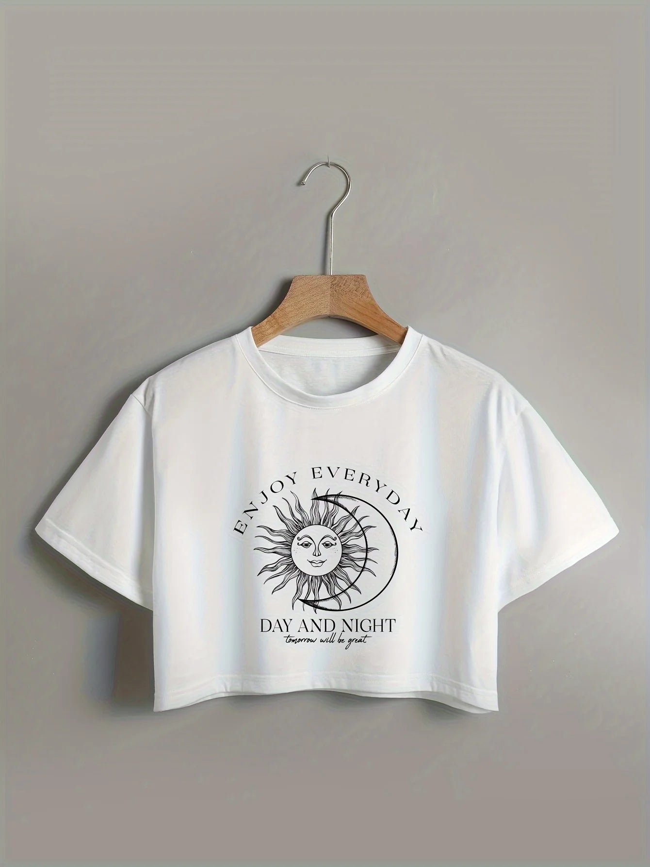 White t-shirt with sun and moon graphic and text on a hanger against a gray background