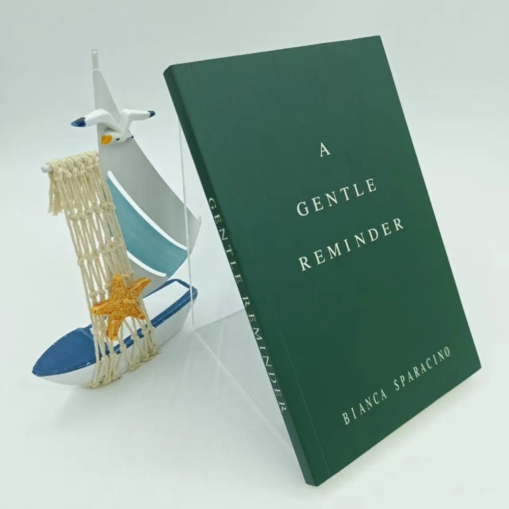 Book titled 'A Gentle Reminder' by Bianca Sparacino with a small model sailboat and starfish on a light gray background.