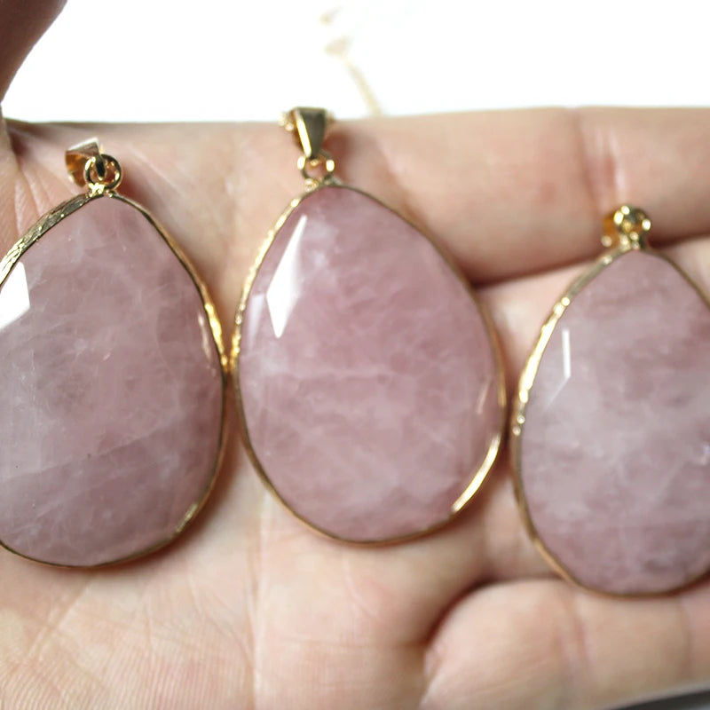 Three pink teardrop-shaped stones with gold settings held in a hand.
