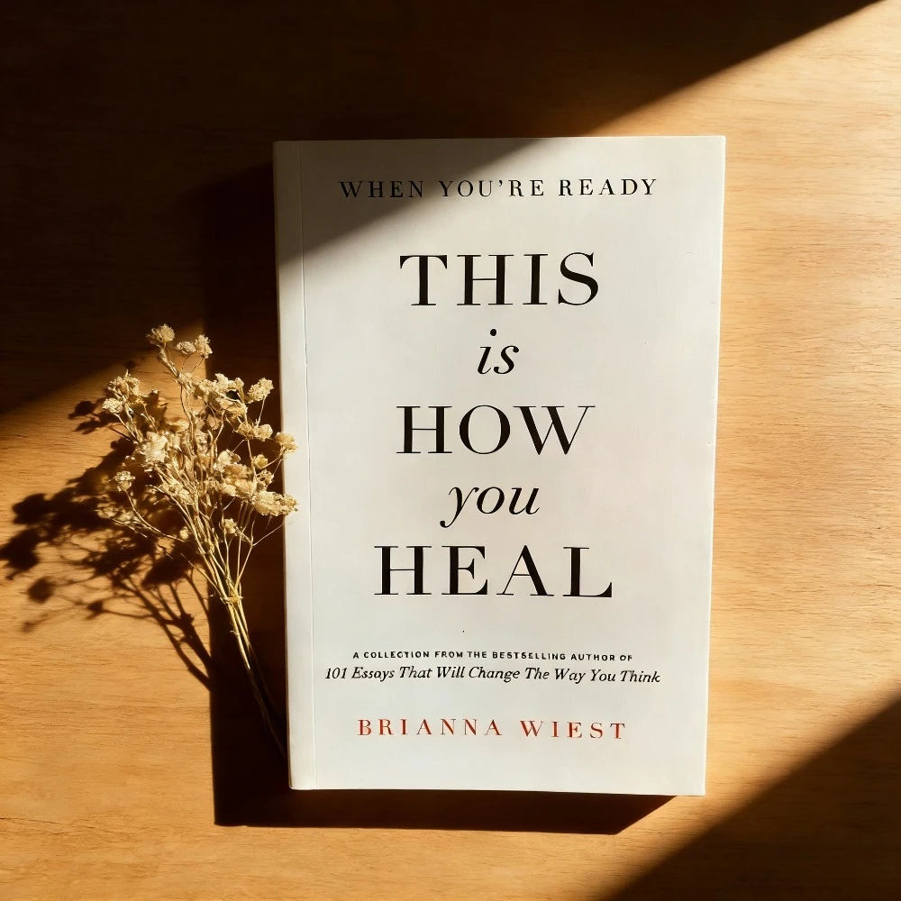 Book titled 'This is How You Heal' by Brianna Wiest on a wooden surface with dried flowers.
