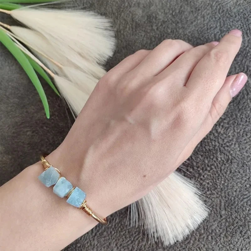 Hand wearing a blue gemstone bracelet on a textured surface with dried grasses.