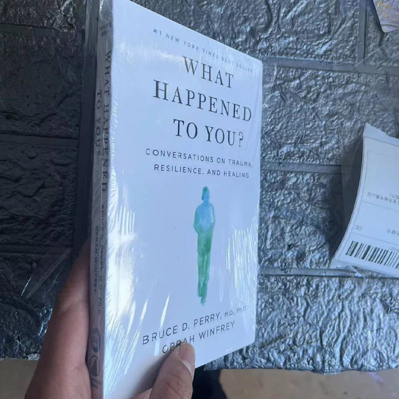 Book titled 'What Happened to You?' held by a hand against a textured wall.