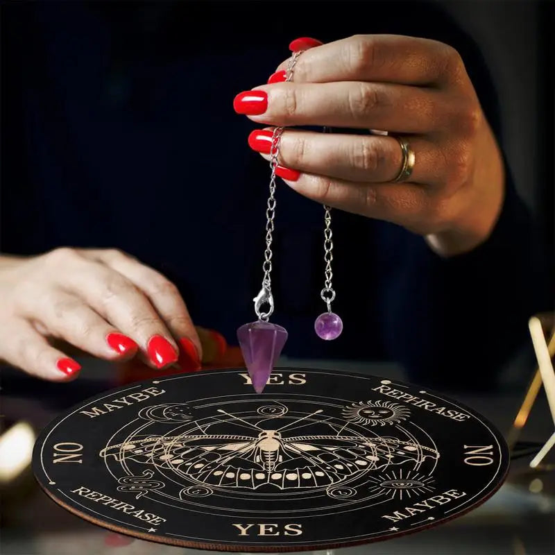 Hand holding pendulum over a divination board with 'YES' and 'NO' options.