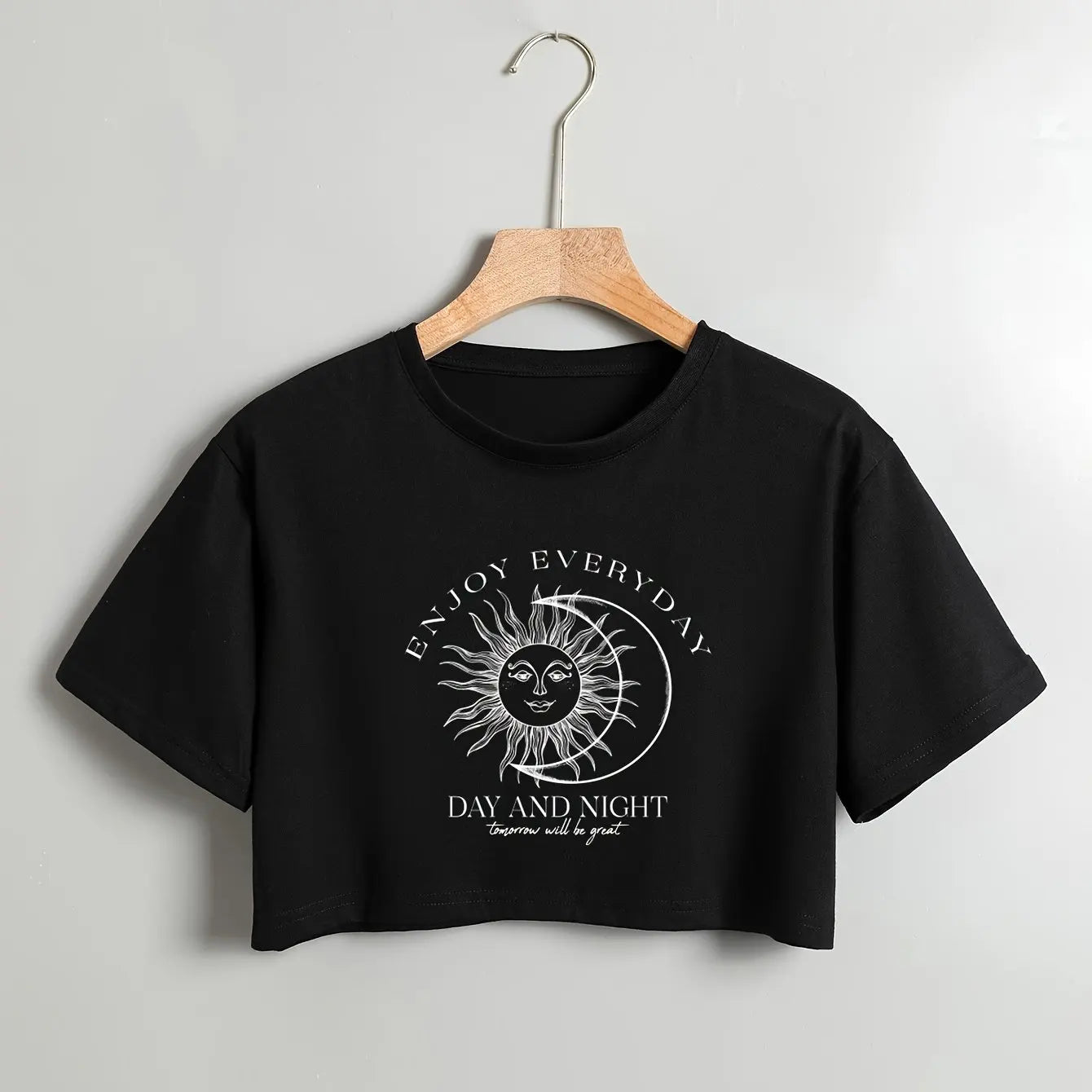 Black crop top with sun and moon design and text on a hanger against a gray background